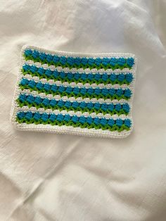 a crocheted dishcloth with green and white stripes on it sitting on a bed