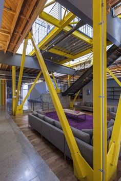 the interior of a large building with yellow metal beams and couches in front of it