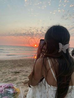 a woman standing on top of a sandy beach next to the ocean with a cell phone in her hand