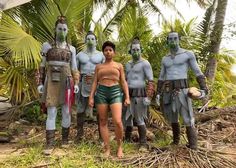 a woman standing in front of statues of men with green paint on their faces and body