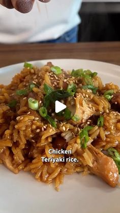 a person is holding chopsticks over a plate of noodles with chicken and green onions