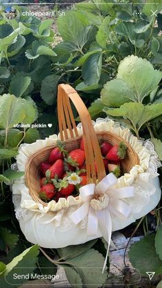 strawberries are in a basket with a bow on the handle, and green leaves behind it