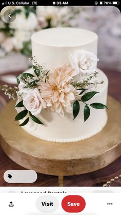 a white wedding cake with pink flowers on top and greenery in the middle, sitting on a wooden stand