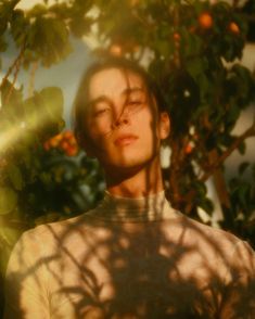 a man standing in front of a tree with his eyes closed and the sun shining on him