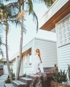 a woman in white dress walking up steps to a house with palm trees behind her