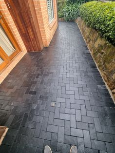 someone's feet are standing on the black brick walkway in front of their house