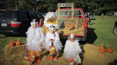 three scarecrows are standing in front of a truck with hay and pumpkins