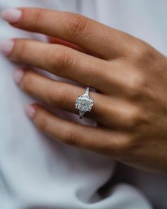 a woman's hand with a diamond ring on her left hand, wearing a white shirt