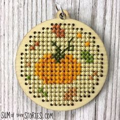 a cross stitch pumpkin ornament hanging on a wooden surface