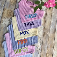 five towels with different words on them sitting next to a pink flower in a vase