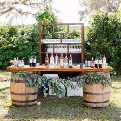 an outdoor bar set up with wine glasses and bottles on top of wooden barrels, surrounded by greenery