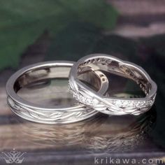 two wedding rings sitting on top of a table next to each other with leaves in the background