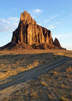 a dirt road in the desert with a mountain in the backgrouund and blue sky