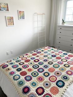 a crocheted granny blanket on top of a bed in a room with white walls