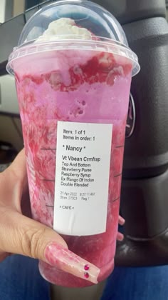 a person holding up a pink drink in their hand with information on the cup sleeve