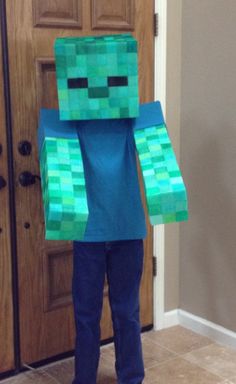 a young boy wearing a minecraft creeper costume standing in front of a door