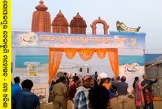 people are standing in front of a stage with an orange drape on the beach