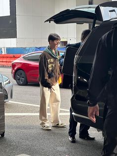 a man standing in the middle of a parking lot next to a car with its trunk open