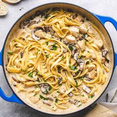 a pan filled with pasta and mushrooms on top of a table next to bread slices