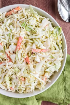 a white bowl filled with coleslaw on top of a green napkin next to silverware