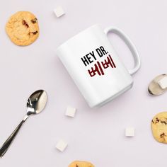 a white coffee mug sitting on top of a table next to cookies and spoons