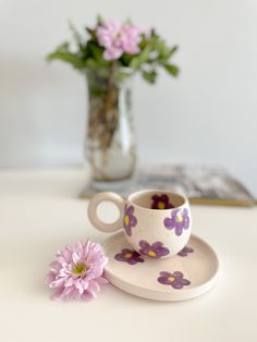 a cup and saucer sitting on a table next to a flower vase