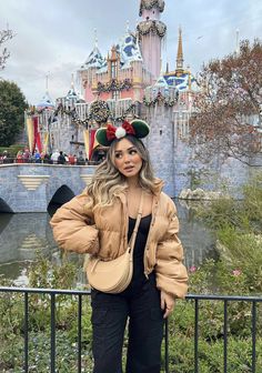 a woman standing in front of a castle with minnie ears on it's head