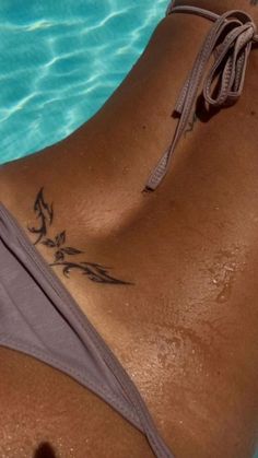 a woman with a tattoo on her back laying next to a swimming pool