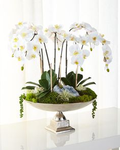 an arrangement of flowers in a bowl on a table with moss and rocks inside it