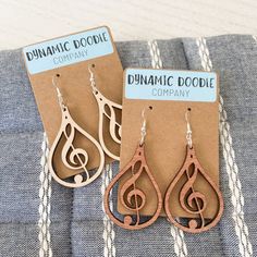 two wooden earrings with musical notes on them are sitting on a piece of fabric next to a card that says dynamic doodle company