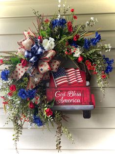 a patriotic wreath on the side of a house with an american flag and red white and blue flowers