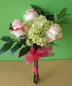 a vase filled with white and pink flowers sitting on top of a wooden table next to a green wall