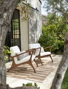 two white chairs sitting on top of a wooden deck next to a tree in front of a house