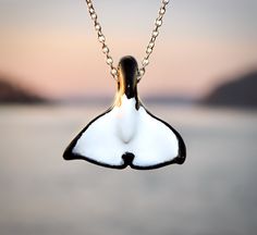 a black and white necklace hanging from a chain on a lake with mountains in the background