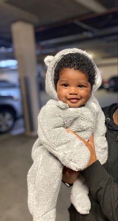 a person holding a baby in a bear costume at an indoor parking lot with cars parked behind them