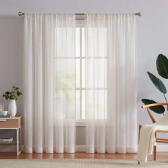 two pack white curtains in the corner of a living room with a chair and potted plant