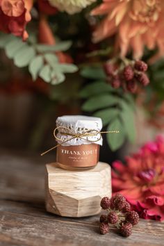 a jar of honey sitting on top of a wooden block with flowers in the background