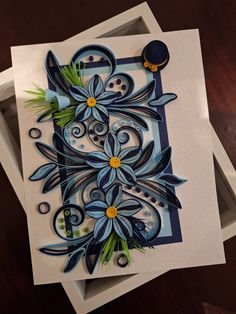 an intricately designed greeting card with blue flowers and green leaves on the front, sitting on a wooden table