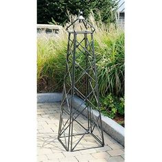 a tall metal plant stand sitting on top of a brick walkway next to some grass