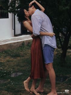 a man and woman standing next to each other in front of a tree with their arms around each other