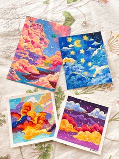 four cards with different designs on them sitting on a tablecloth, one has an image of the sky and clouds