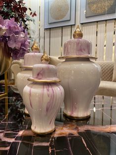 three white vases sitting on top of a marble table next to a purple flower