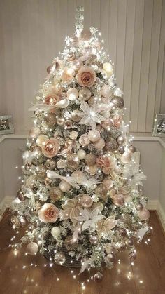 a white christmas tree with pink and silver ornaments on the top is lit up by fairy lights