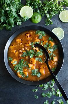 a black bowl filled with soup and garnished with cilantro, limes, and parsley