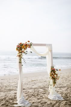 an outdoor wedding setup on the beach with white draping and orange floral arrangements