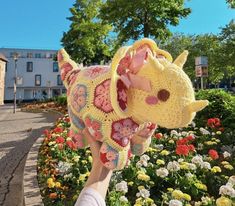 a person is holding up a stuffed animal in front of flowers and buildings on a sunny day