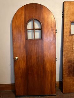 two wooden doors with arched glass windows next to each other on the floor in front of a white wall