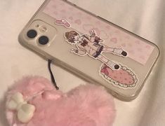 a pink teddy bear laying on top of a bed next to a cell phone case