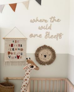 a baby crib with a stuffed giraffe in the corner and wall hangings above it