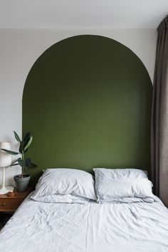 a bed with white sheets and pillows in front of a green headboard on the wall